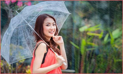 young Thai lady standing with under umbrella under rainning