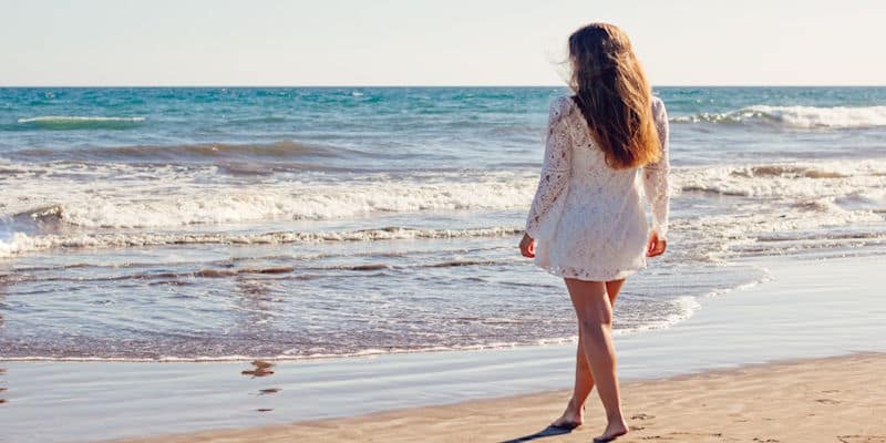 Woman walking barefoot along a peaceful beach shoreline, enjoying a quiet moment by the ocean as a way to reduce everyday stress.
